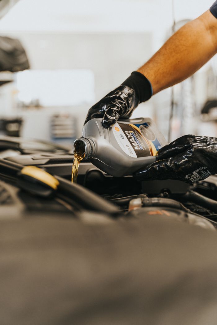 Crafting Captivating Headlines: Your awesome post title goes here Close-up of a mechanic pouring engine oil into a car engine with gloved hands, indoors.