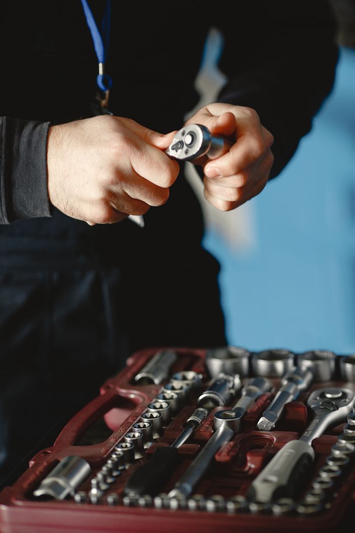 About Auto mechanic in workshop holding a wrench over a toolbox with various tools.